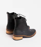 Botas acordonadas estilo borcego, confeccionadas en cuero vacuno negro. Presentan detalles de perforaciones decorativas tipo brogue en la puntera y laterales, con suela y taco de madera en tono natural.