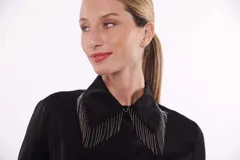 Camisa color beige con cuello clásico, cierre frontal con botones y detalle de flecos metálicos en el cuello.