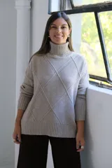 Polerón de cuello alto con diseño de rombos tejidos en relieve, mangas largas con puños acanalados y ruedo también acanalado.