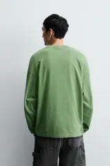 Camiseta de manga larga con corte relajado y cuello redondo, confeccionada con un acabado de efecto lavado. Presenta un estampado frontal con tipografía gótica y números en contraste.