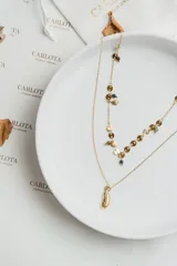 Collar doble de acero dorado con dije de pluma y cuentas de colores.