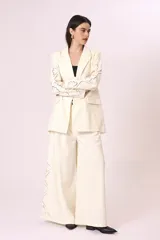 Blazer color crema con solapas de muesca, cierre frontal con dos botones, bolsillos delanteros con solapa y mangas largas con bordados calados.