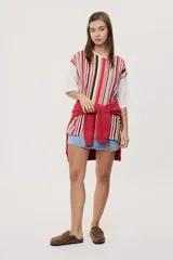 Remera oversize de manga corta con diseño de rayas verticales en tonos rojos, negros, blancos y tostados, y mangas blancas lisas.