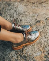 Zapato acordonado estilo oxford de cuero vacuno en color plateado metalizado, con diseño brogue, suela de goma y taco de madera.