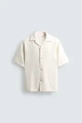 Camisa de manga corta y calce relajado, confeccionada en tejido seersucker con textura. Presenta cuello bowling y cierre frontal de botones.