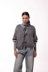 Saco de punto gris con frente abierto, cierre mediante lazos frontales y mangas con puños elásticos. Presenta una textura suave y un diseño de volumen holgado.