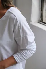 Remera de algodón color blanco, con cuello en V, mangas largas y corte holgado con costuras visibles en el ruedo.