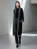 Cardigan largo de punto marca Via Milano, color negro con detalles de rayas blancas en contraste. Presenta un diseño abierto sin botones, bolsillos frontales aplicados y ribetes blancos en la apertura, puños y bolsillos.