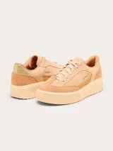 Championes Sorel modelo Ona Ave T-Toe, color beige con detalles en gamuza y cuero. Presenta suela de plataforma con diseño estriado y detalle metálico dorado en el talón.