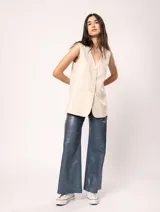 Chaleco color crema de lino con corte sastrero, largo a la cadera, forro interno, botones delanteros, silueta levemente entallada y tajo cruzado en la espalda.