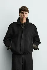 Cazadora cropped fit color verde militar, confeccionada en tejido efecto ante. Cuenta con cuello solapa, manga larga con puño abotonado, trabillas en los hombros, bolsillos laterales ocultos y un bolsillo interior. El bajo tiene elástico interior y el cierre frontal es con cremallera oculta por solapa con botones a presión.