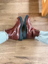 Botas de cuero color marrón rojizo con diseño estilo brogue, cierre lateral y suela track negra de goma resistente.