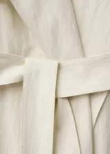 Abrigo largo color crema con cuello de solapa ancha, trabillas en los puños, cinturón desmontable y dos bolsillos laterales.