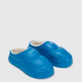 Pantuflas tipo zueco de diseño acolchado, color azul vibrante, con interior forrado en piel sintética blanca y logo de la marca estampado en el empeine.