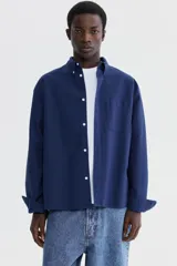 Camisa de manga larga H&M de corte relajado, confeccionada en algodón Oxford azul marino. Cuenta con cuello americano, bolsillo aplicado en el pecho y botones frontales blancos.