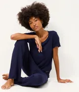 Pijama de dos piezas compuesto por una blusa de manga corta con escote redondo y un pantalón largo de corte recto con cintura elástica. La prenda presenta un bordado sutil en el pecho y un acabado liso.