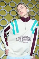 Buzo color crema con cuello alto y cierre frontal parcial. Presenta bloques de color en turquesa y bordó en los hombros y mangas, y un estampado frontal con la frase "SLOW WEEKEND SPORTY MOOD" en bordó.