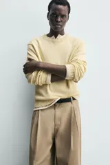 Pantalón chino de corte wide fit confeccionado en tejido de algodón. Presenta pliegues frontales, bolsillos laterales y bolsillos traseros de vivo, con cierre frontal de cremallera y botón.
