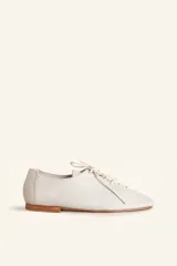 Zapato tipo chata de cuero vacuno color crema, con diseño de cordones frontales y suela plana de cuero.
