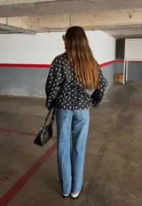Campera de algodón con estampado de lunares blancos sobre fondo negro. Presenta cuello alto, cierre frontal con botones metálicos y cinturón ajustable en la cintura. Posee bolsillos laterales y un diseño versátil que permite llevarla entallada o con silueta holgada.
