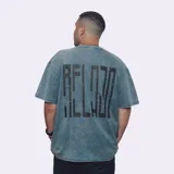 Remera de manga corta, corte oversize, color azul con efecto acid wash o distorsión. Presenta un pequeño texto bordado o estampado en el pecho.