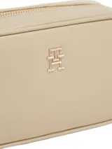 Cartera tipo camera bag de Tommy Hilfiger en color beige, con acabado liso y cierre de cremallera. Presenta el monograma TH metálico en la parte frontal y cuenta con una correa ajustable y extraíble.