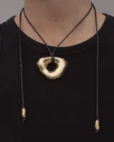 Collar con dije de forma irregular en tonos dorados y plateados, suspendido de un cordón doble de algodón negro.