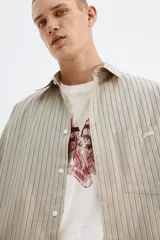 Camisa de popelina de algodón con cuello inglés, tapeta clásica y bolsillo superior abierto. Presenta un canesú en la espalda y mangas largas con puños abotonados. El bajo es levemente redondeado.