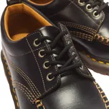 Zapatos de cuero negro Dr. Martens modelo Lowell, con puntera moc toe, costuras contrastantes amarillas y suela gruesa acanalada.