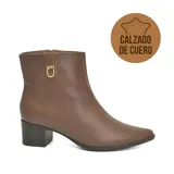 Bota corta de cuero color marrón, con taco cuadrado de altura media y punta fina. Presenta un detalle metálico dorado con el logo de la marca en el lateral y cierre lateral.