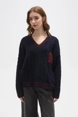 Sweater de tejido de punto con diseño de trenzas, cuello en V y detalles de rayas en contraste en cuello, puños y ruedo. Presenta un número bordado en el frente y tiene un corte holgado.