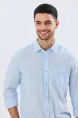 Camisa de lino de manga larga en color beige, con cuello camisero, cierre frontal de botones y un bolsillo ojal en el pecho.
