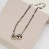 Collar de doble cadena fina de acero color plateado con un dije central en forma de símbolo de infinito. La cadena tiene un extensor con eslabones más grandes.