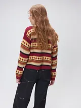 Campera de punto estampada de corte holgado, con cierre metálico frontal y cuello de corderito sintético en color tostado. Presenta un diseño de franjas horizontales con patrones geométricos en tonos bordó, mostaza, marrón y beige.