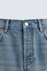 Jeans de mezclilla rígida de algodón, color azul claro con efecto lavado y ligero desgaste. De tiro medio, corte recto desde la cadera hasta la rodilla y ligeramente acampanado en el bajo (bootcut). Cierre frontal con botonadura y cinco bolsillos.