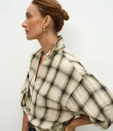Blusa de viscosa con estampado de cuadros en tonos beige y verde. Presenta cuello en V, cierre frontal con botones y mangas 3/4 abullonadas con puños elásticos.