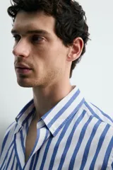 Camisa de corte regular fit confeccionada en tejido de algodón, con diseño de rayas verticales en azul y blanco. Presenta cuello solapa con botones, cierre frontal de botones, manga larga con puños abotonados y un bolsillo en el pecho.
