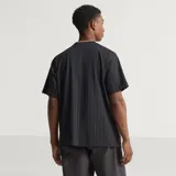 Camiseta de fútbol Adidas del Manchester United, modelo Terrace Icons. Diseño negro con sutiles rayas verticales moradas, franjas amarillas en los hombros y detalles bordados en dorado, incluyendo el trébol de Adidas y el escudo clásico del club.