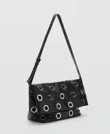 Bolso tipo tote de color negro, confeccionado en poliuretano, con diseño de ojales metálicos plateados distribuidos por toda la superficie y asas largas para llevar al hombro.