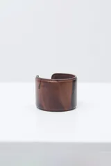 Brazalete rígido de cuero marrón con costuras decorativas en los bordes y diseño abierto.