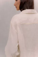 Camisa de lino blanca con cuello tradicional, manga larga, cierre frontal con botones y un bolsillo en el pecho con detalle bordado.