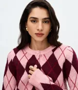 Cardigan corto de punto con estampado de rombos en tonos rosado y bordó, cuello redondo, mangas largas y cierre frontal con botones revestidos.
