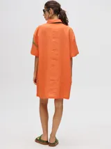 Camisa tipo vestido de corte oversize, confeccionada en viscosa. Presenta un diseño estampado con trazos abstractos en tonos verdes sobre una base naranja, cuello clásico, cierre frontal con botones y mangas cortas.