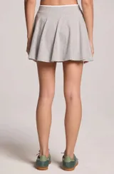 Pollera short corta de color gris melange, confeccionada en algodón. Presenta una silueta relajada y fluida con diseño acampanado y cintura elástica ajustable mediante cordón blanco.