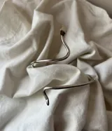 Brazalete rígido plateado con forma de serpiente enroscada.