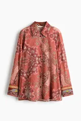 Camisa de manga larga confeccionada en gasa de algodón con estampado tipo paisley y motivos ornamentales en tonos rojizos y rosados. Presenta cuello clásico, cierre frontal con botones y puños abotonados.