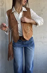 Chaleco de gamuza color camel con bordados en hilo crudo a lo largo de los bordes delanteros, diseño floral bordado en el lateral, tachas metálicas decorativas y botones a presión ocultos.