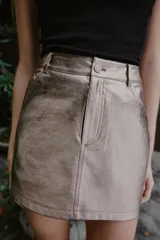 Minifalda de corte recto efecto piel en color plateado metalizado, con diseño de cinco bolsillos, trabillas para cinturón y cierre frontal con cremallera y botón metálico.