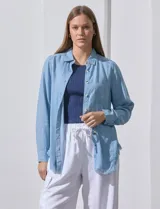 Camisa celeste de tencel, marca Hester & Orchand. Tiene cuello con solapa, escote en V, abertura central con botones, bolsillo aplicado en el frente y ruedo desflecado.