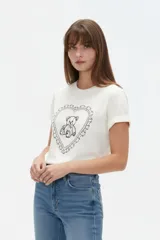 Remera de manga corta de algodón color blanco, con cuello redondo y estampado frontal de un oso dentro de un corazón con volados.